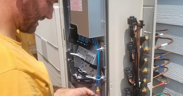 Technician working on the wiring and refrigerant connections of an outdoor unit