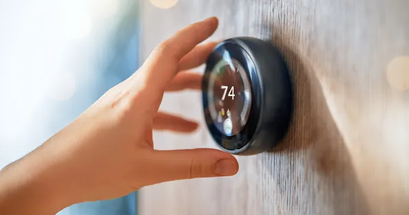 Hand adjusting a smart thermostat set to 74 degrees
