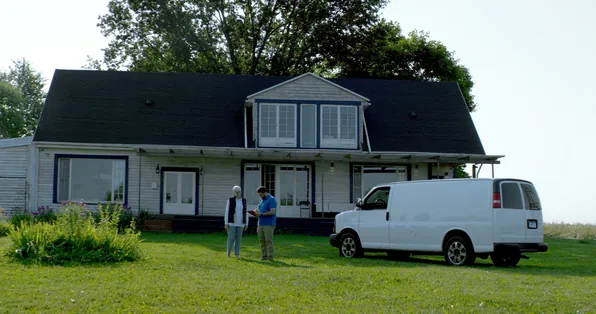 Two people talking on the lawn of a two-story home beside a white service van
